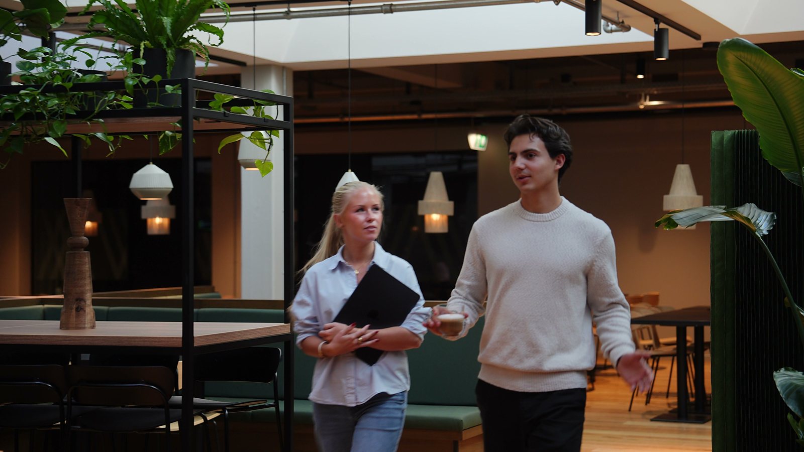 Two colleagues walking through the lounge with a coffee and a laptop