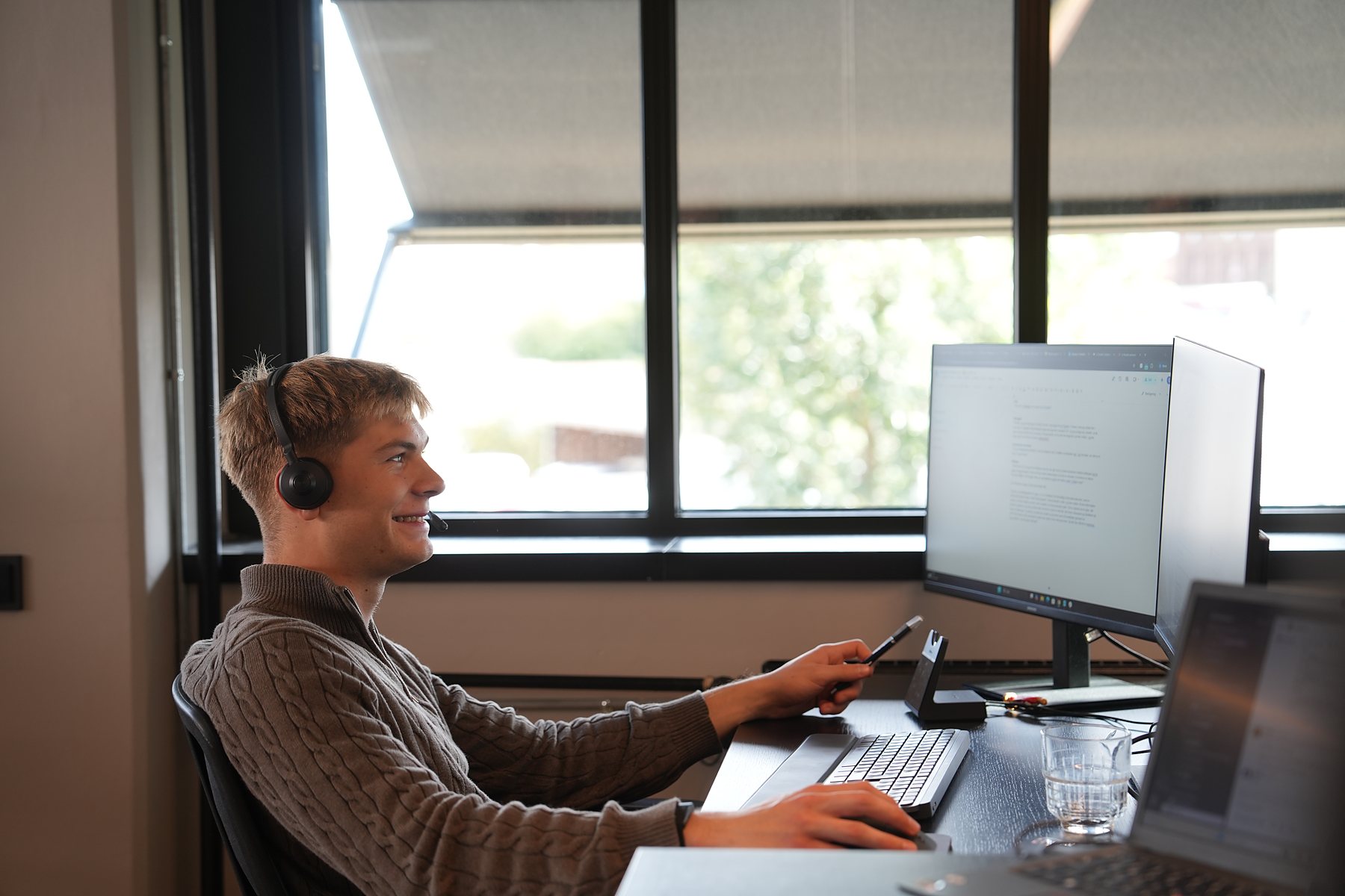 An SDR in a headset laughing mid-call by the window