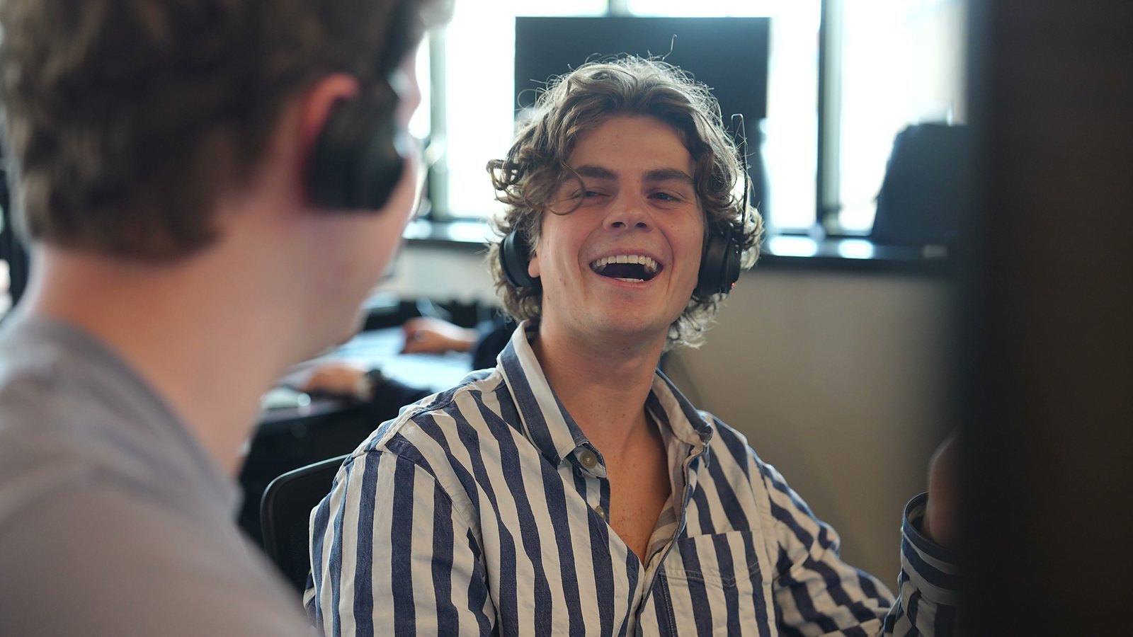 SDR i stribet skjorte griner højlydt med en kollega