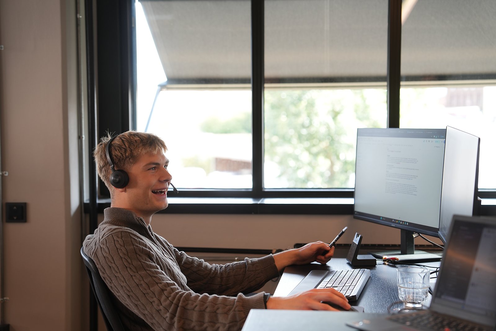 SDR med headset smiler midt i et opkald ved vinduet