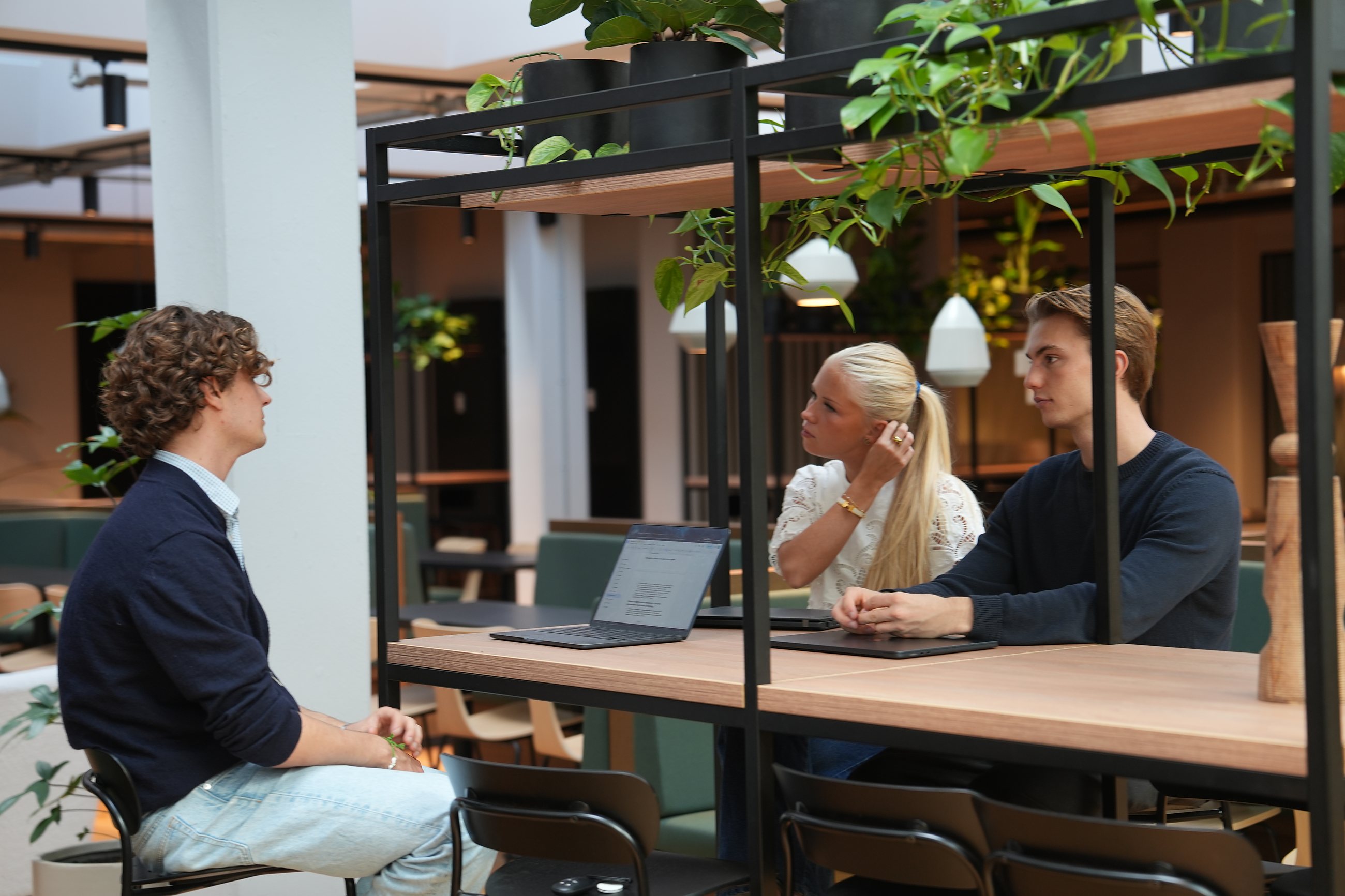 A meeting seen through the glass wall: two talking at the table, a colleague in the foreground